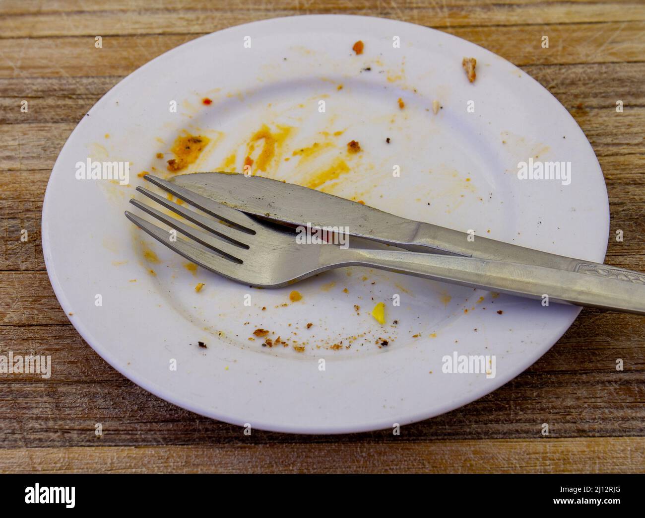 An empty dinner plate after a meal isolated on a wood surface Stock