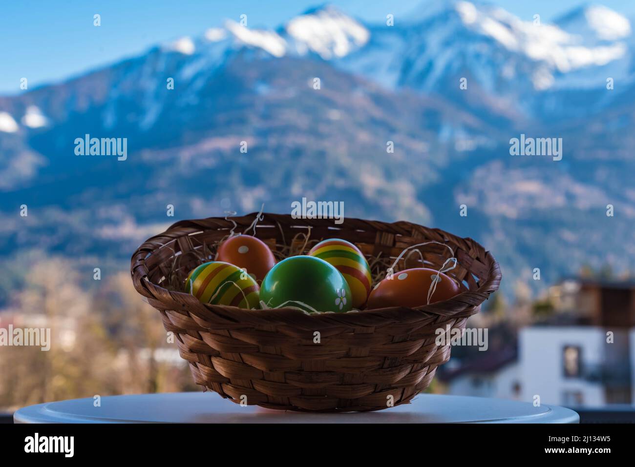 close up exposure of handmade easter basket with colorful easter eggs in a nest and wonderful snowy mountain backdrop in the tyrolean alp Stock Photo