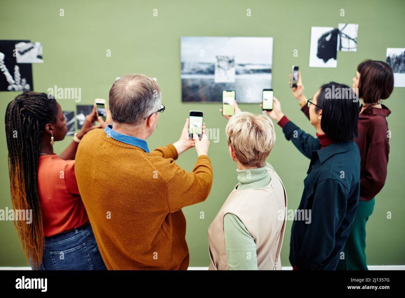 Group of multi-ethnic visitors scanning QR code to get more information about black and white photo on wall at exhibition in museum Stock Photo