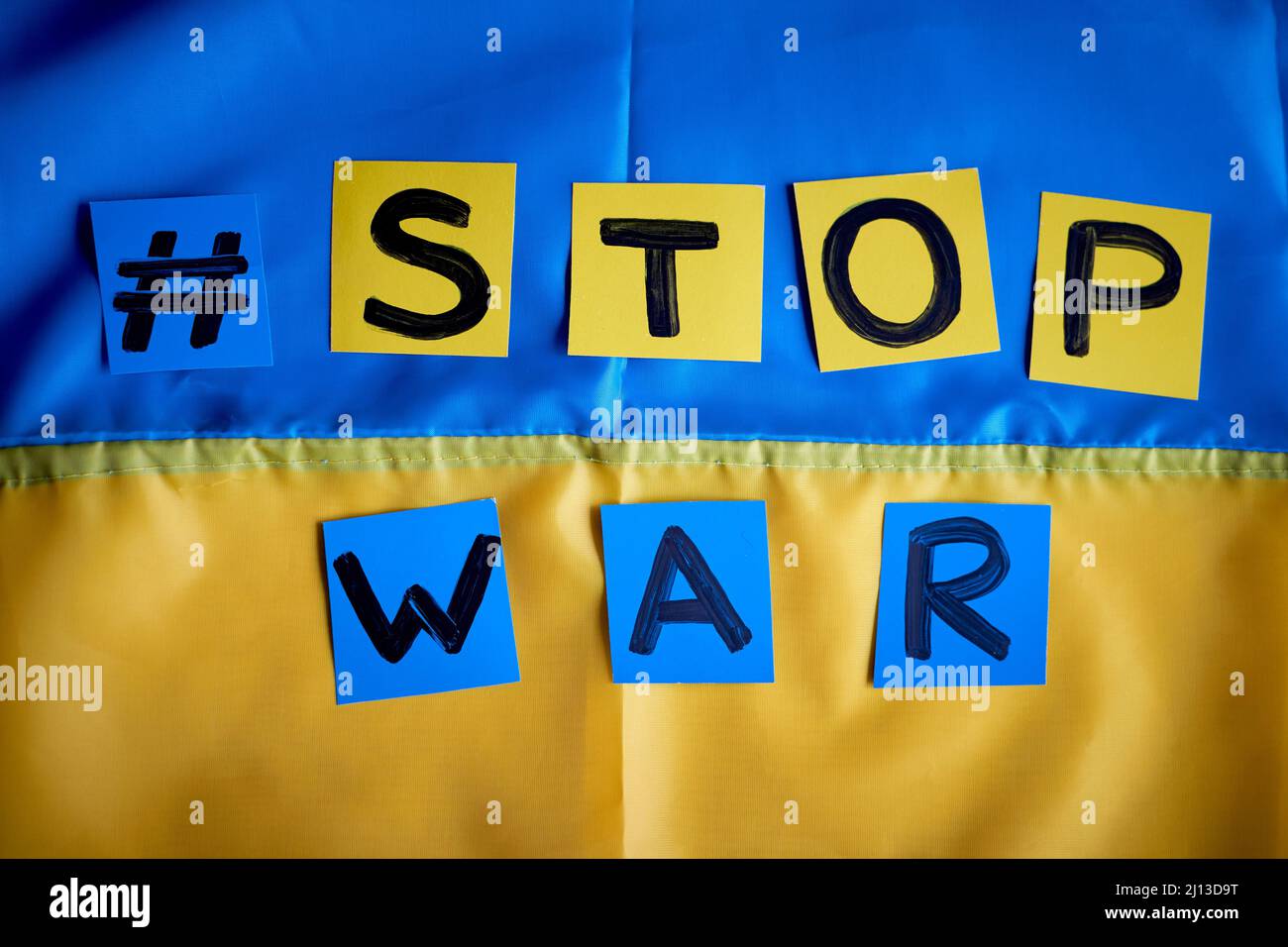Paper drawn banner Stop War hashtag on Ukrainian flag yellow-blue background. Kids support Ukraine, stay with Ukraine Stock Photo