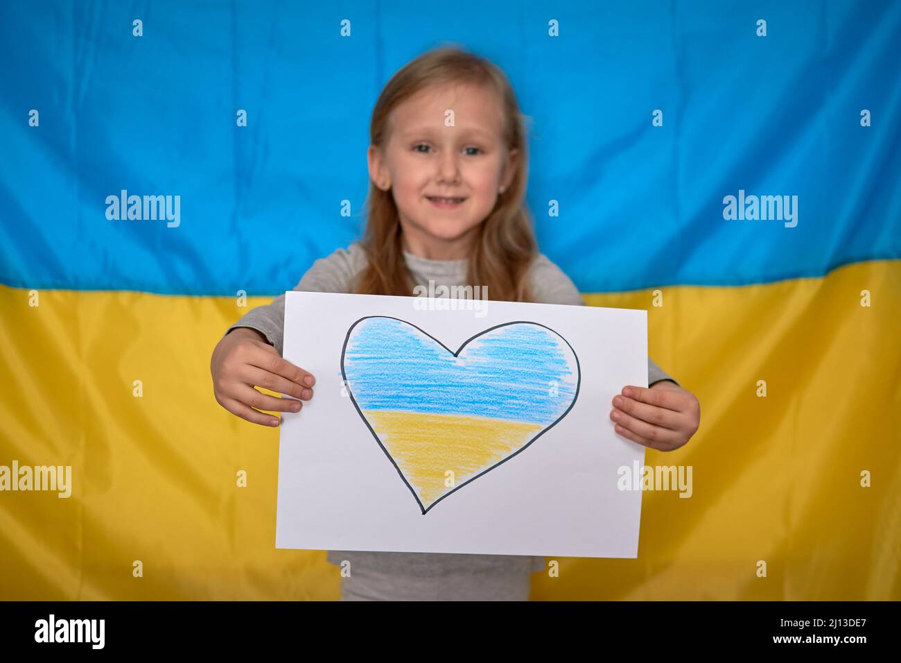 Girl hands holding paper banner with drawn yellowblue heart on