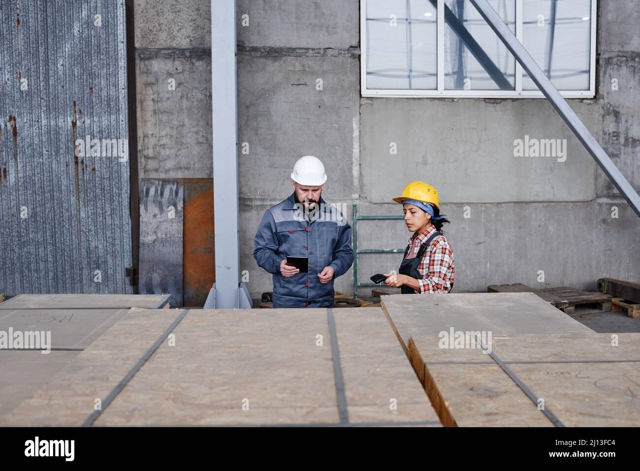 Two workers of distribution warehouse checking barcodes on containers with new spare parts for contemporary industrial machines Stock Photo
