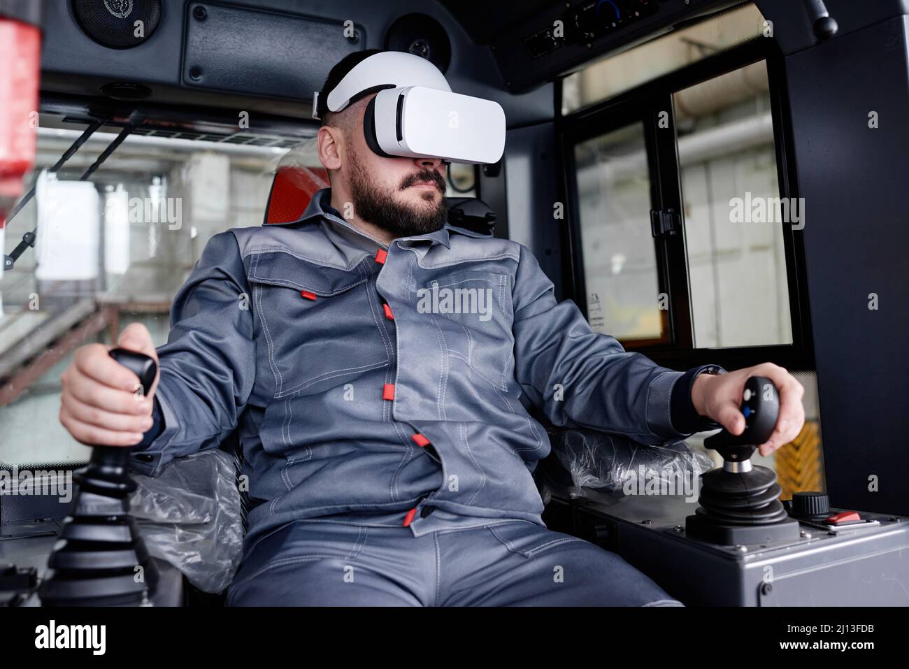 Confident male builder in vr headset and workwear holding by gearshifts while sitting inside construction machine and driving it Stock Photo