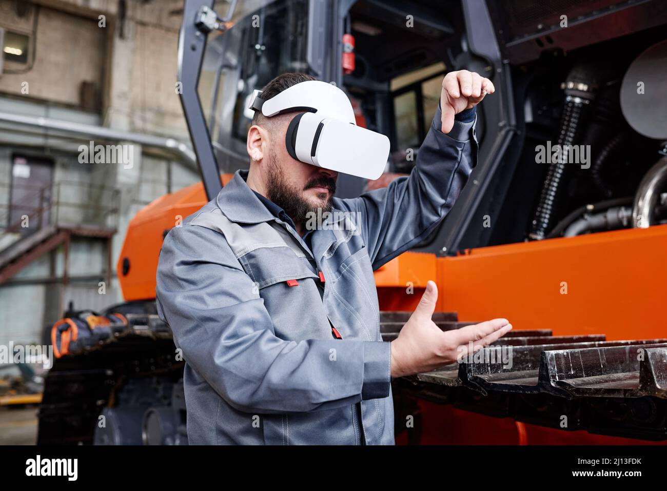 Contemporary engineer in vr headset forming shape of virtual machine by his hands while standing in warehouse or workshop Stock Photo