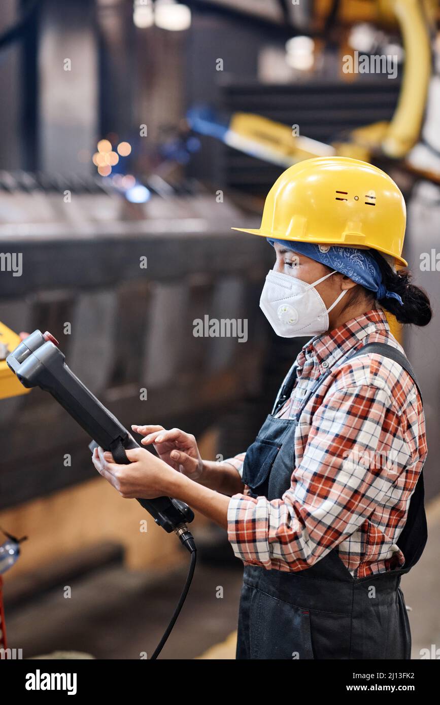 Side view of contemporary technician of factory using switch device to control work of industrial machine in warehouse Stock Photo