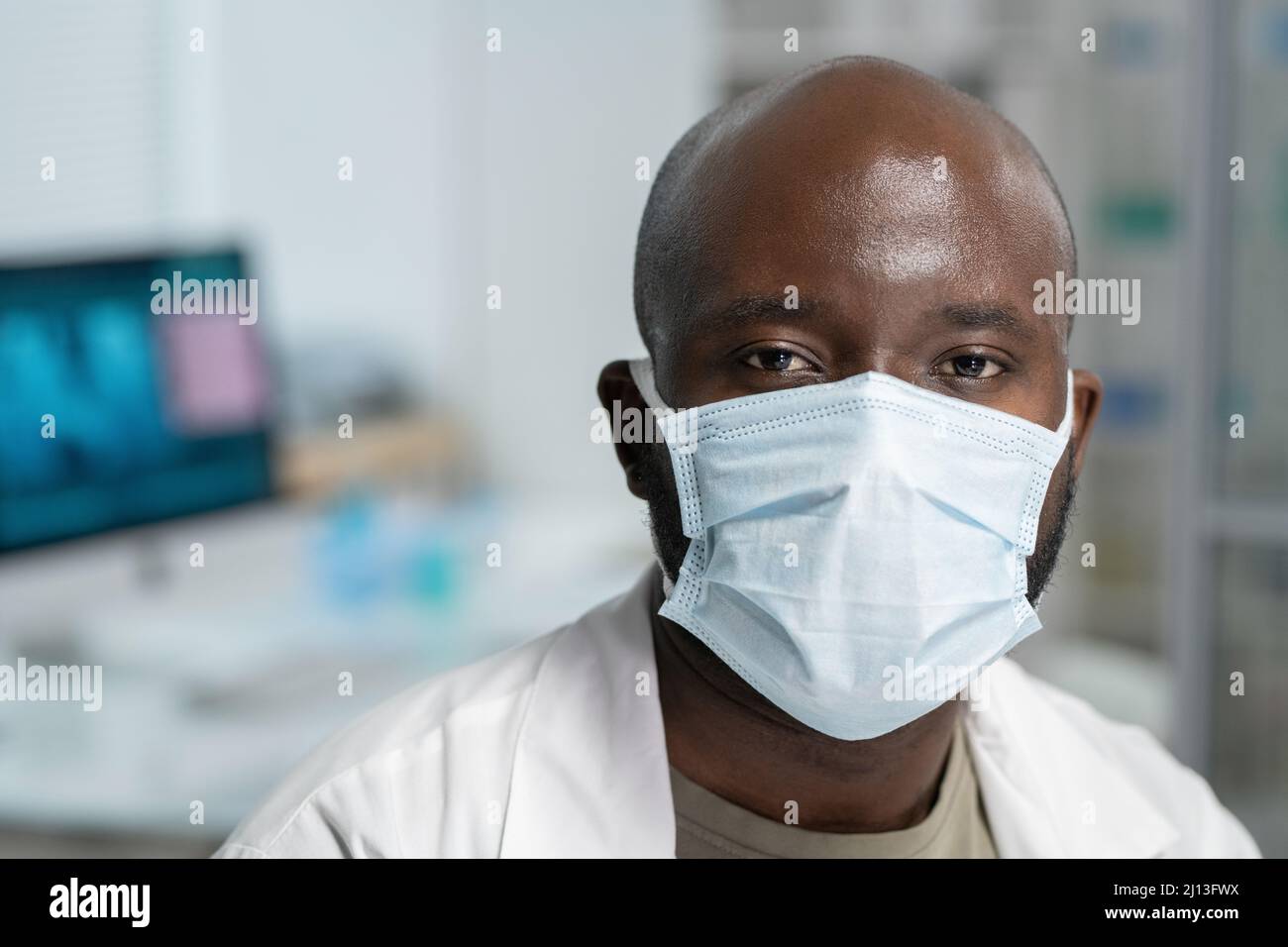 Head of young black man in whitecoat protective mask looking at camera ...