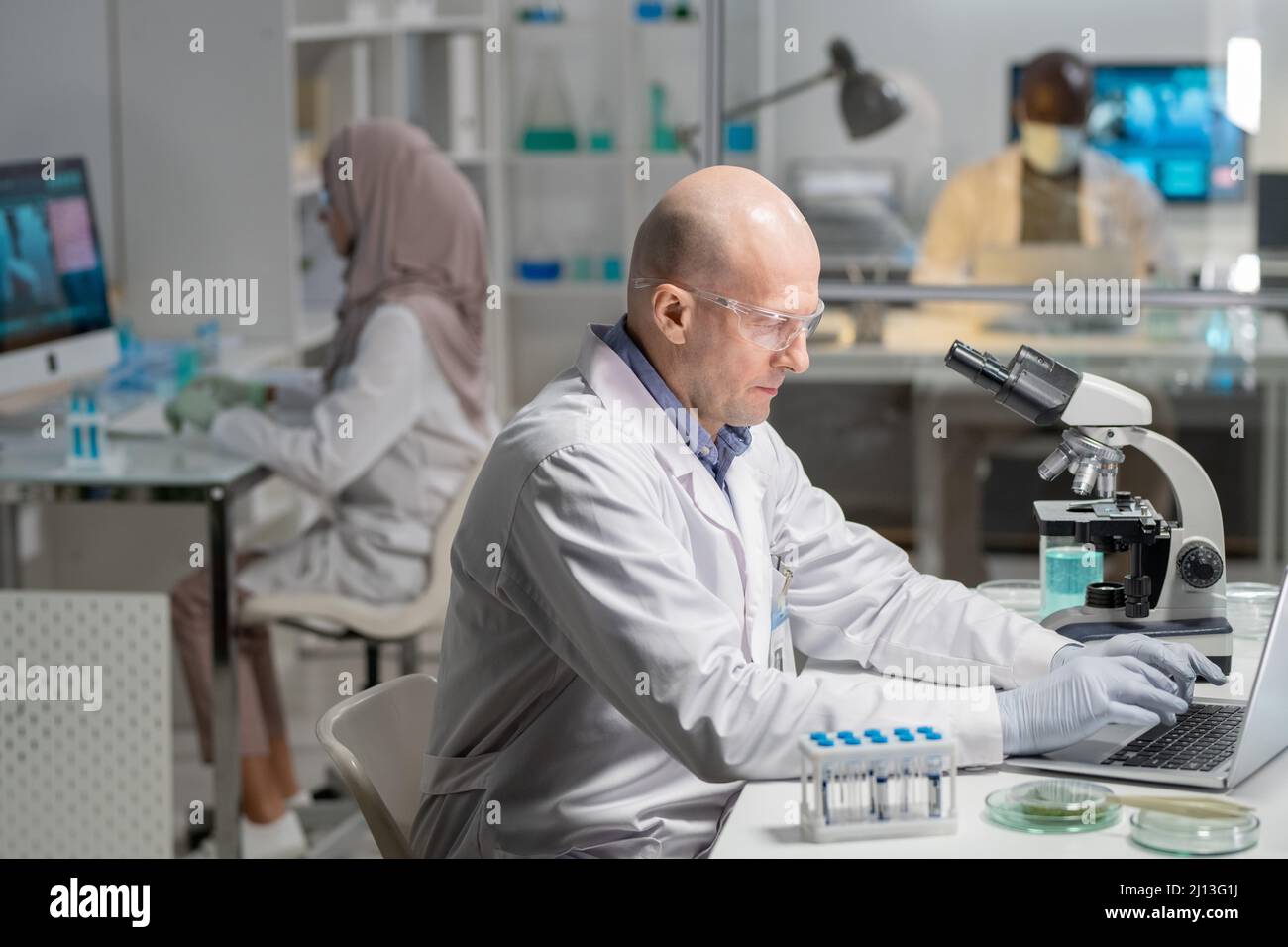 Mature serious male lab worker in gloves, whitecoat and protective eyeglasses searching for scientific information in the net Stock Photo