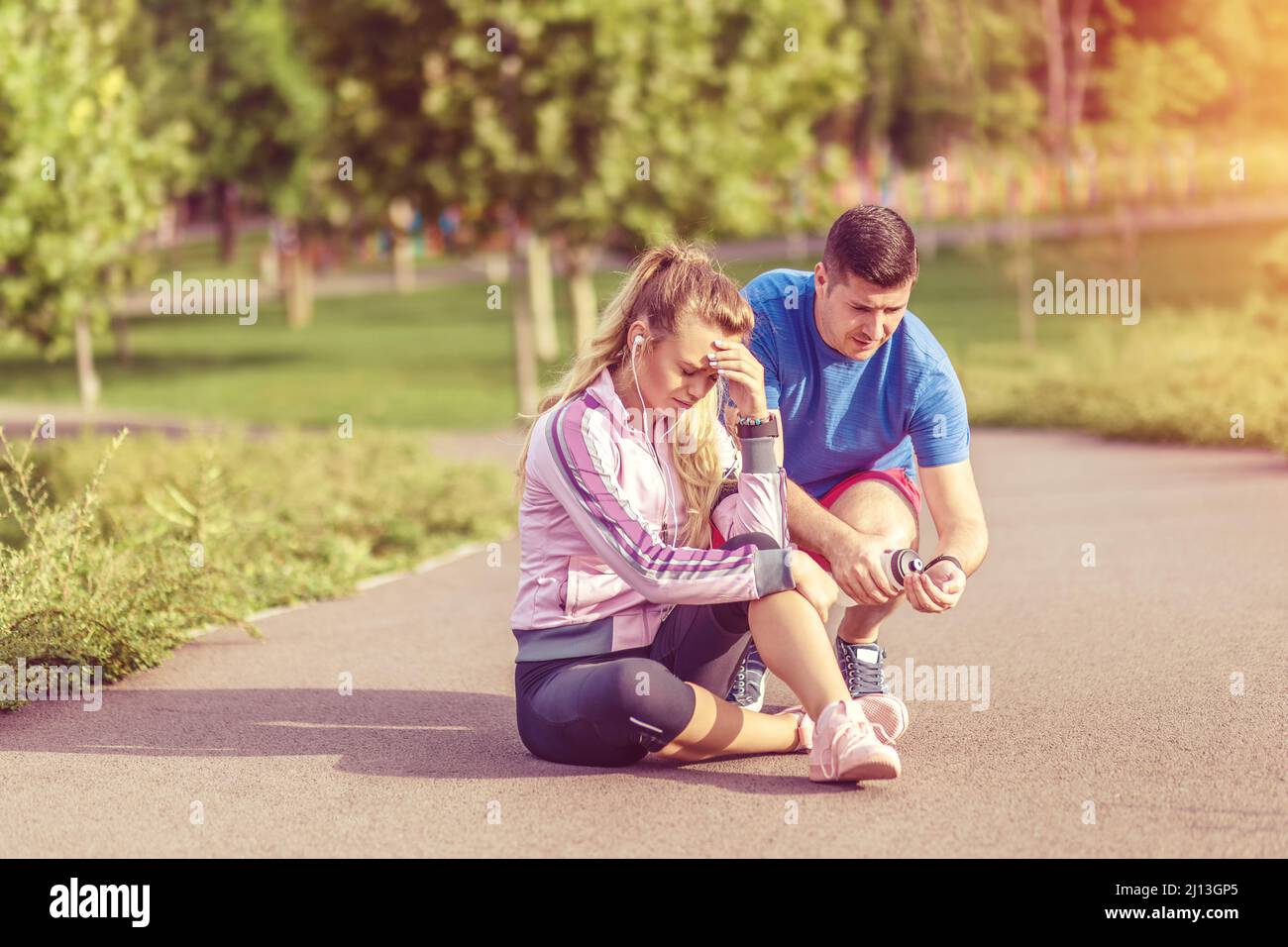 Young woman with knee injury while jogging outdoor helped by her male partner Stock Photo