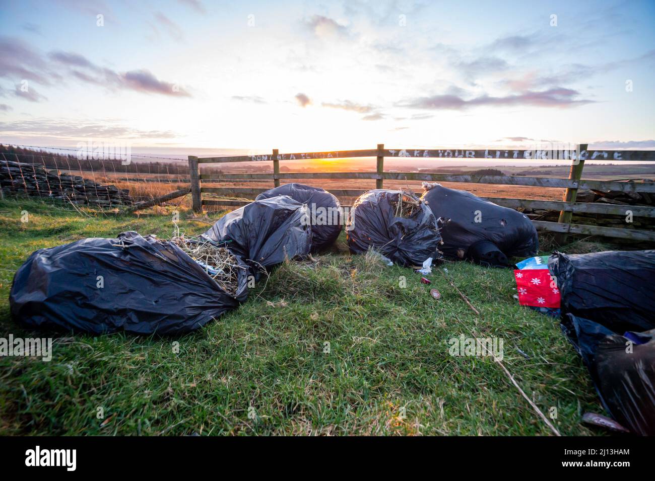 Fly tipping, rubbish dumping in English countryside. Graffiti on the fence reads 'take your litter home'. Stock Photo