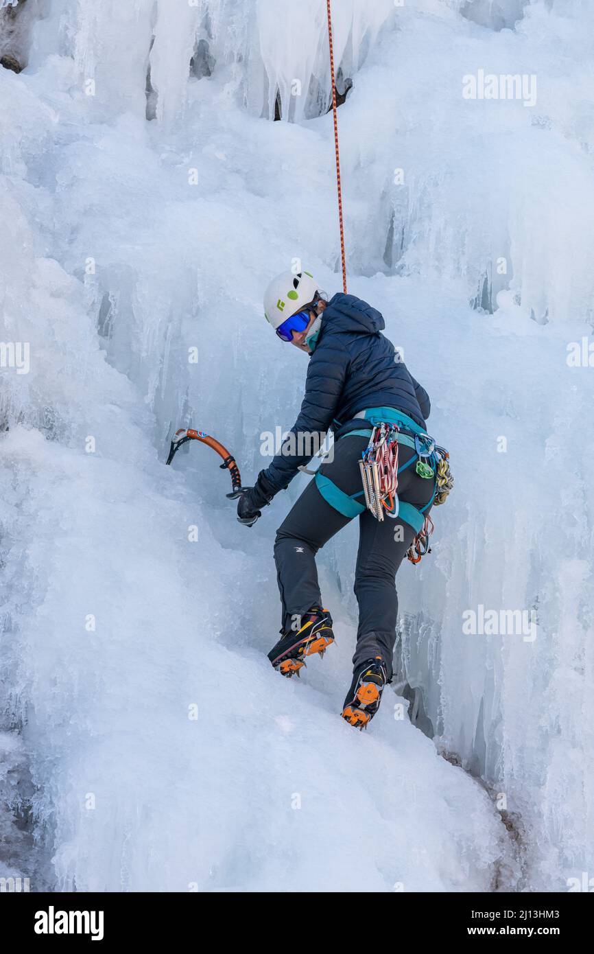A female ice climber ascending an ice wall using ice axes and crampons