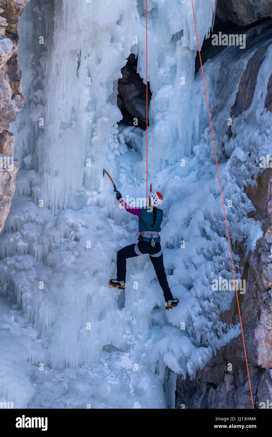 A female ice climber ascending an ice wall using ice axes and crampons
