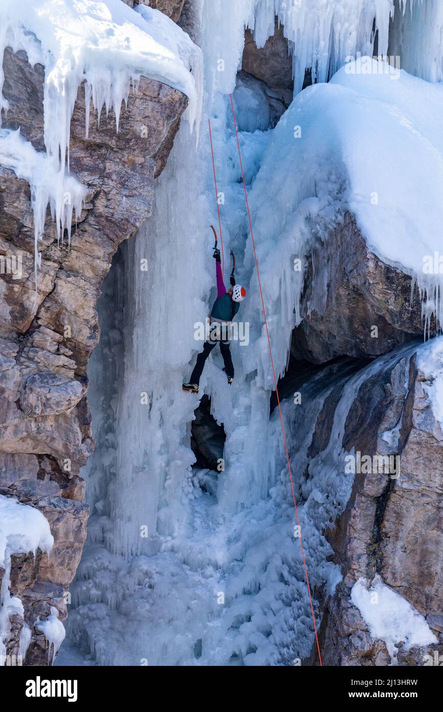 A female ice climber ascending an ice wall using ice axes and crampons