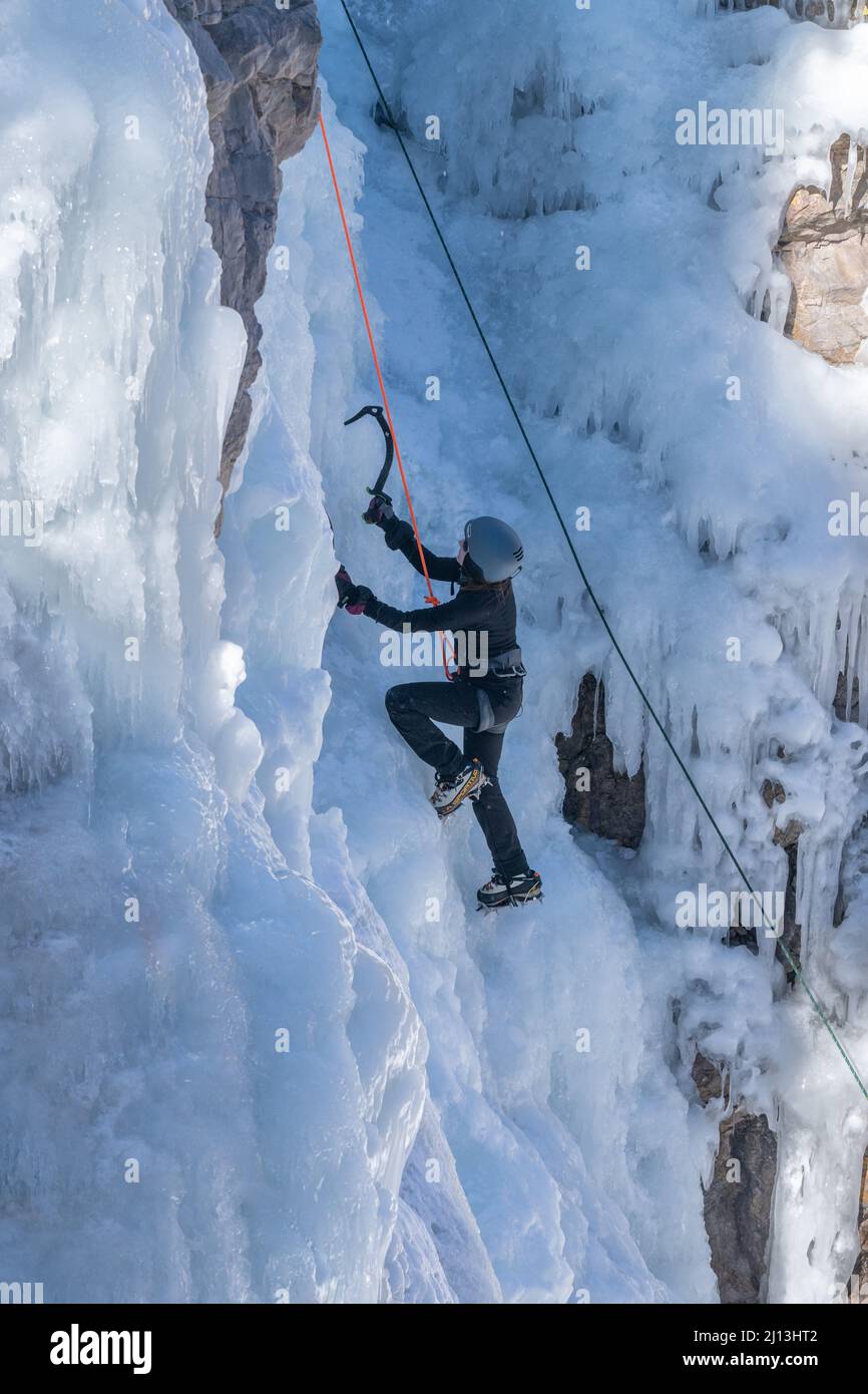 A female ice climber ascending an ice wall using ice axes and crampons