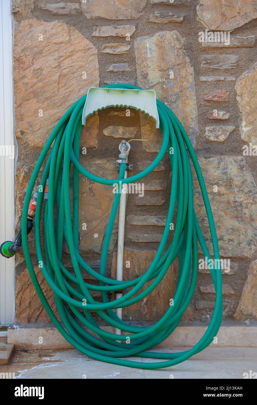 Green long garden hose. Coiled garden hose hanging on faucet against