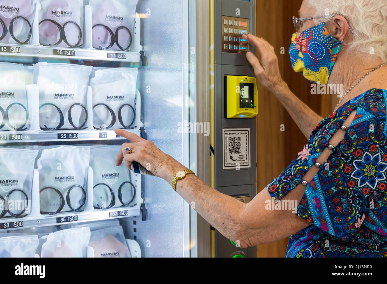 Elderly woman wearing mask purchasing a mask from vending machine to help prevent spread of coronavirus Stock Photo