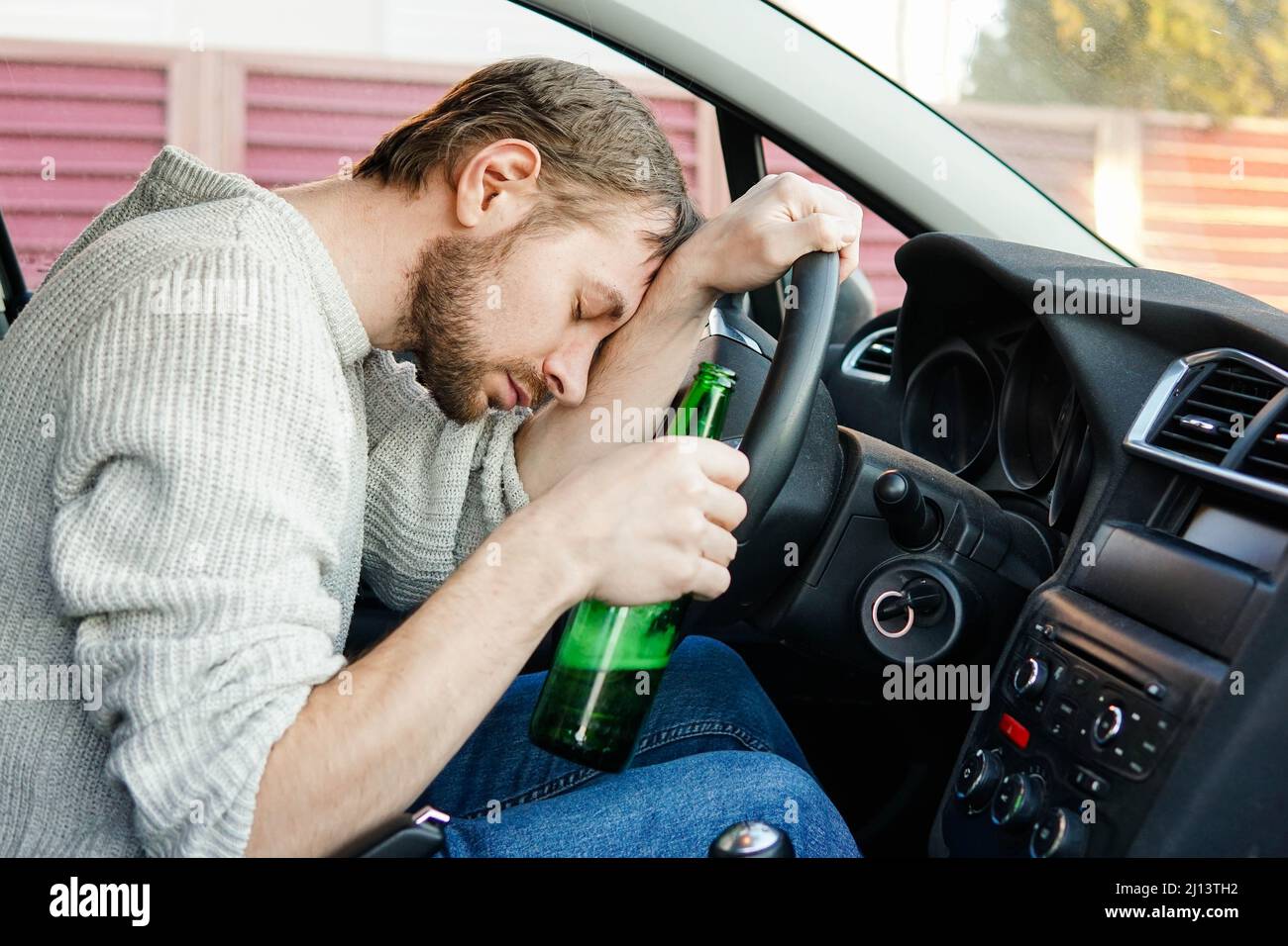 Young drunk man fall asleep behind the wheel of a car. Male car driver holding bottle of beer. Stock Photo