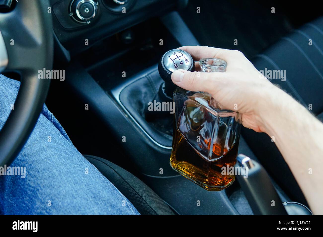 Close up of man driving car and holding bottle of alcohol. Responsibly and safety driving. Stock Photo