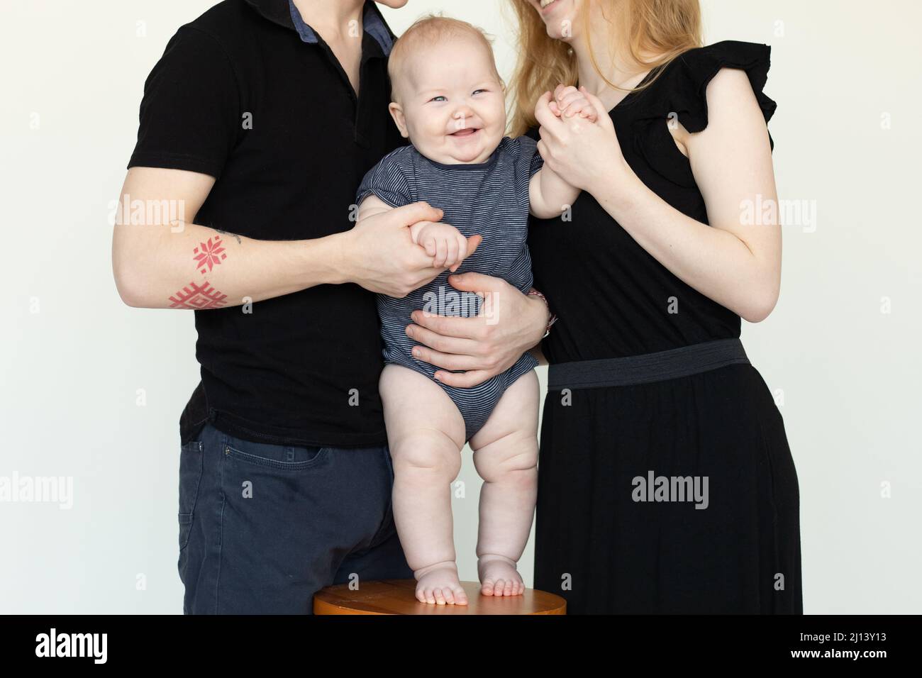 Laughing baby on chair. Cropped photo of traditional full family, standing and embrace together. Caring infant, protect Stock Photo