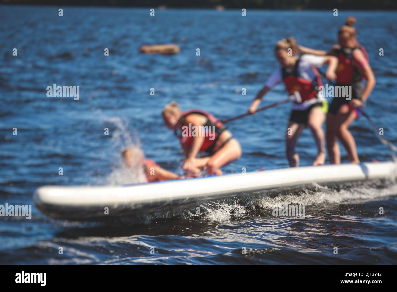 Group of young SUP surfers fall from stand up paddle board, women