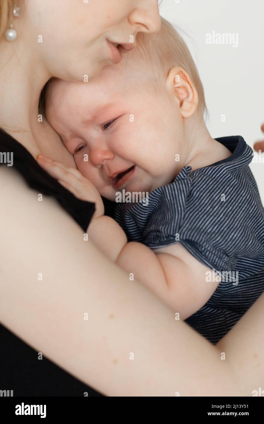 Face of crying child. Mother caring, holding wailing depressed baby in arms. Temperature, illness, kid colic. Close up Stock Photo