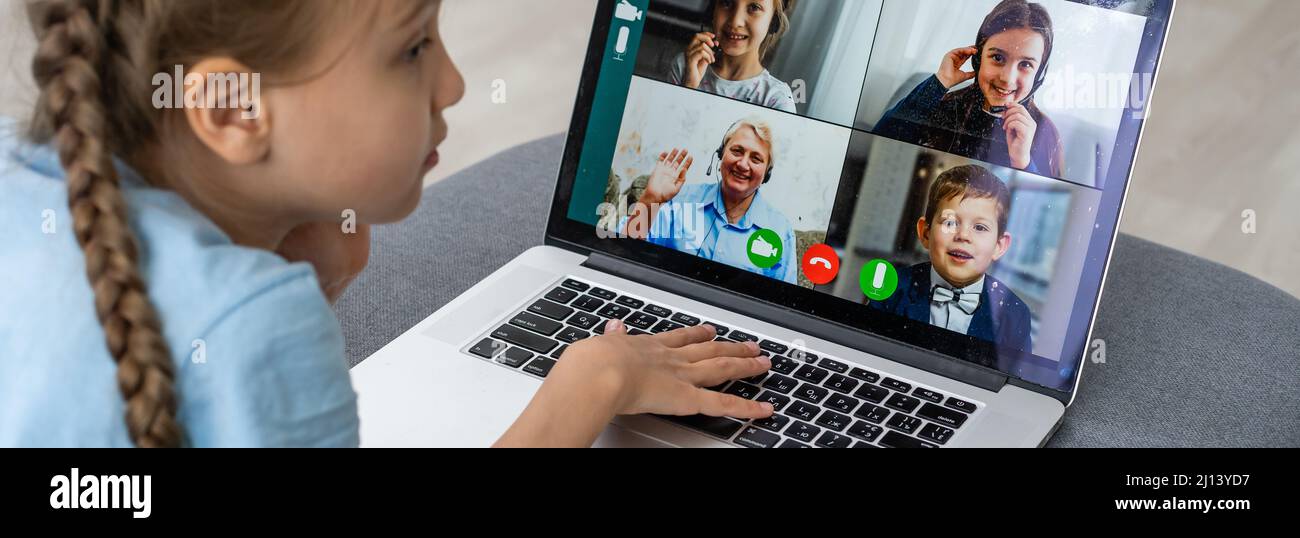 Distance learning. Cheerful little girl girl in headphones using laptop ...