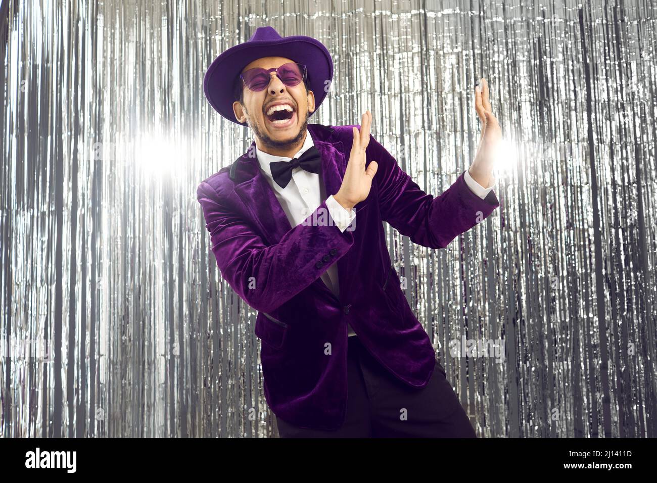 Happy funny goofy man in a purple suit, glasses and hat dancing and laughing at a party Stock Photo