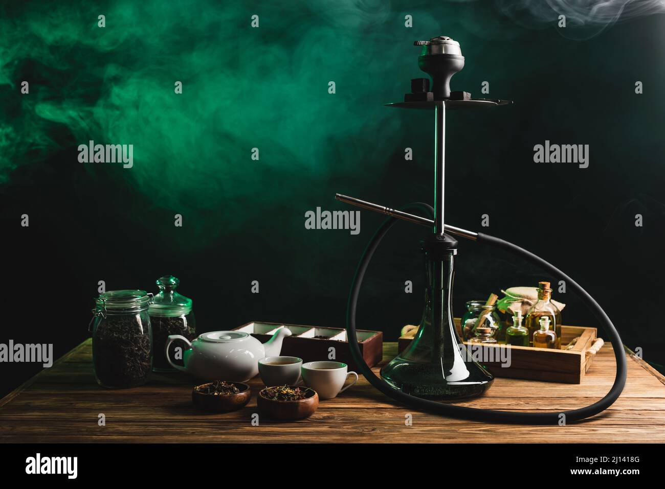 Tea and hookah on wooden table on black background with smoke Stock