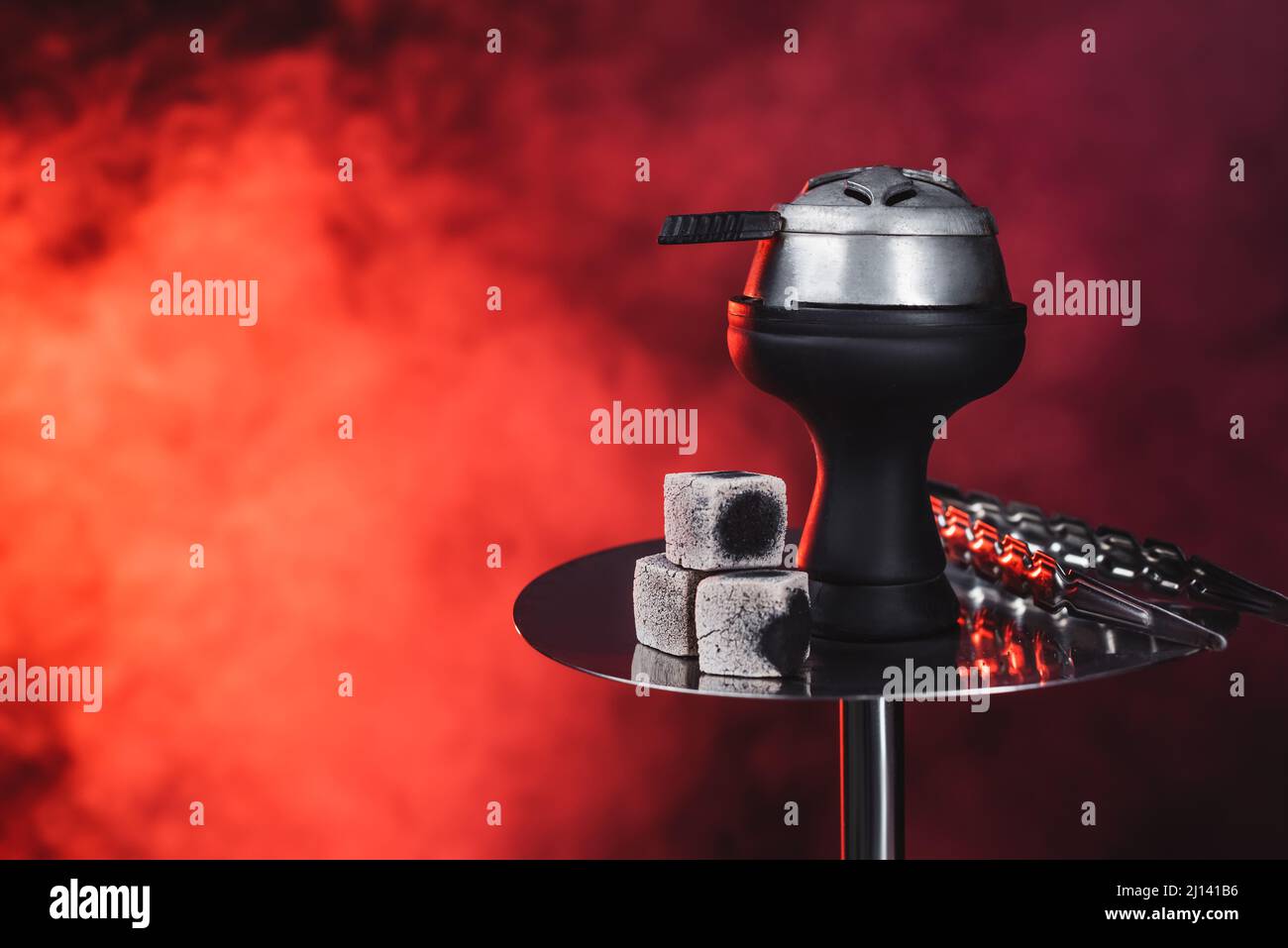 Coals and tweezers on hookah on black background with red smoke Stock