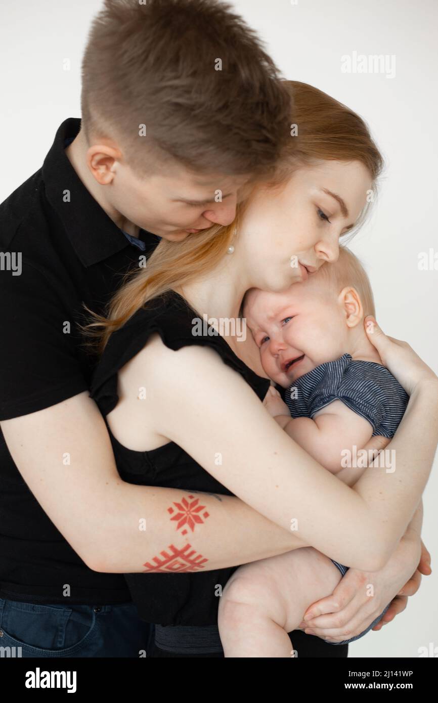 Vertical mom and dad, family caring and holding wailing depressed baby in arms. Temperature because of tooth ache, pain Stock Photo