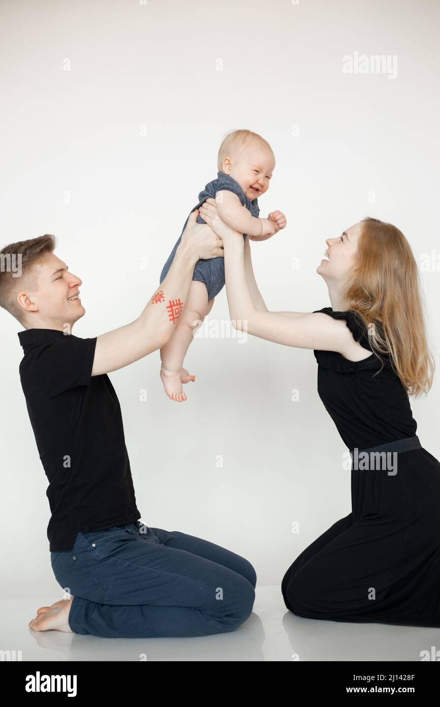 Happy smiling laugh blond family sitting on knee together in studio, playing child in the air. First steps, moves, dance Stock Photo