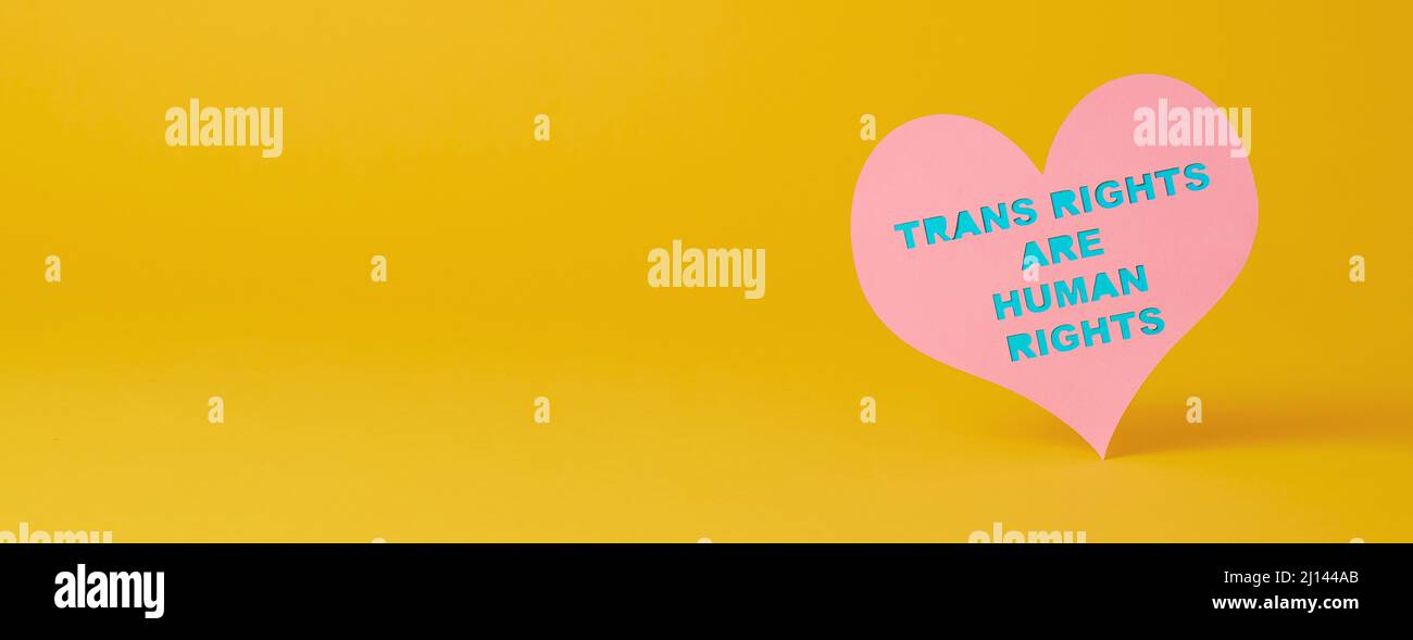 closeup of pink cardboard heart with the text transgender rights are human rights cut out in it, on a yellow background, in a panoramic format to use Stock Photo