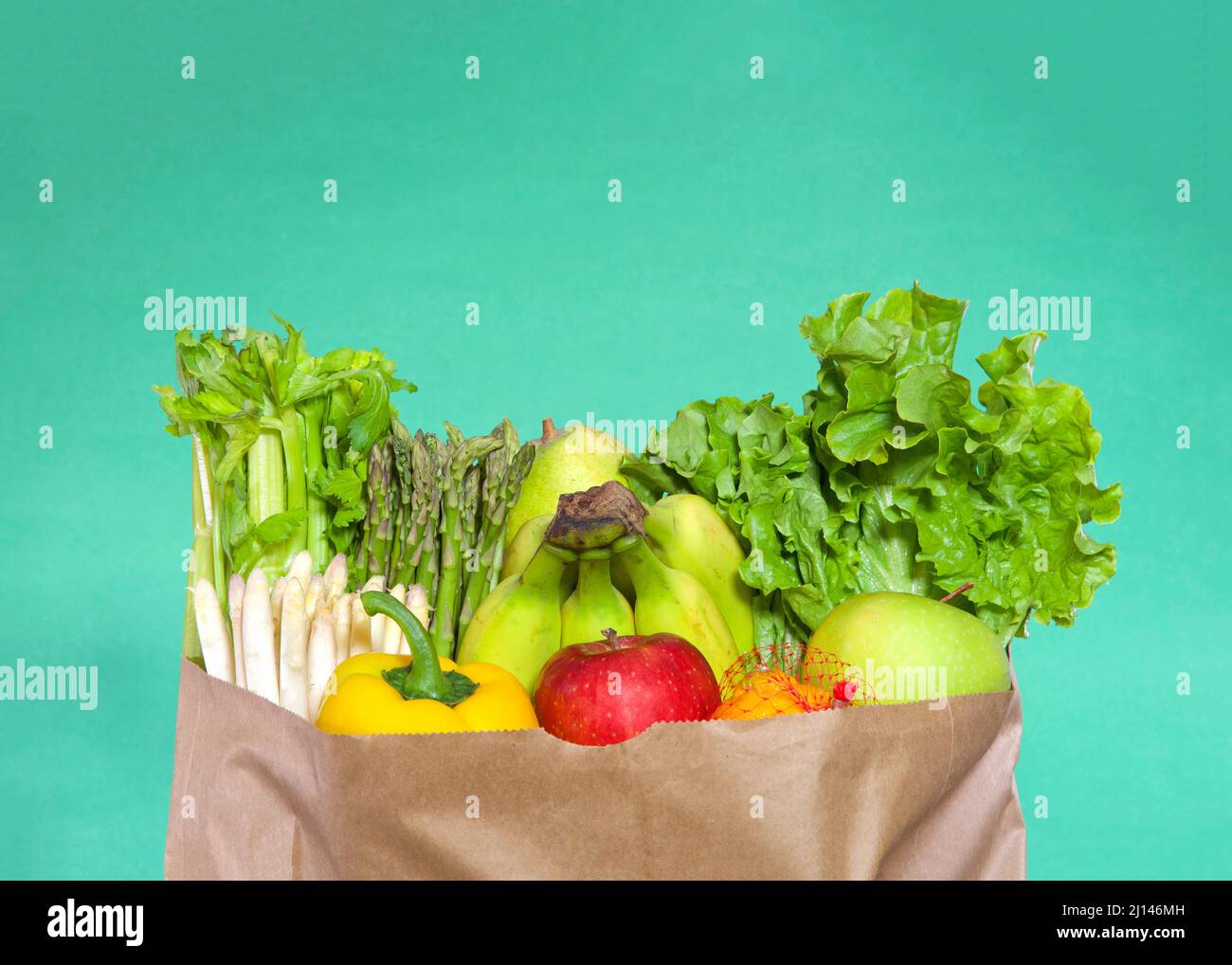 Top of brown paper grocery bag stuffed full with fruits and vegetables. Celery, white and green asparagus, bananas, lettuce, yellow bell pepper, red a Stock Photo