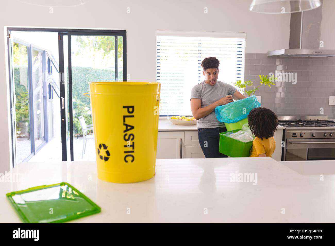 Yellow plastic bucket for recycling against hispanic father teaching son about waste management Stock Photo