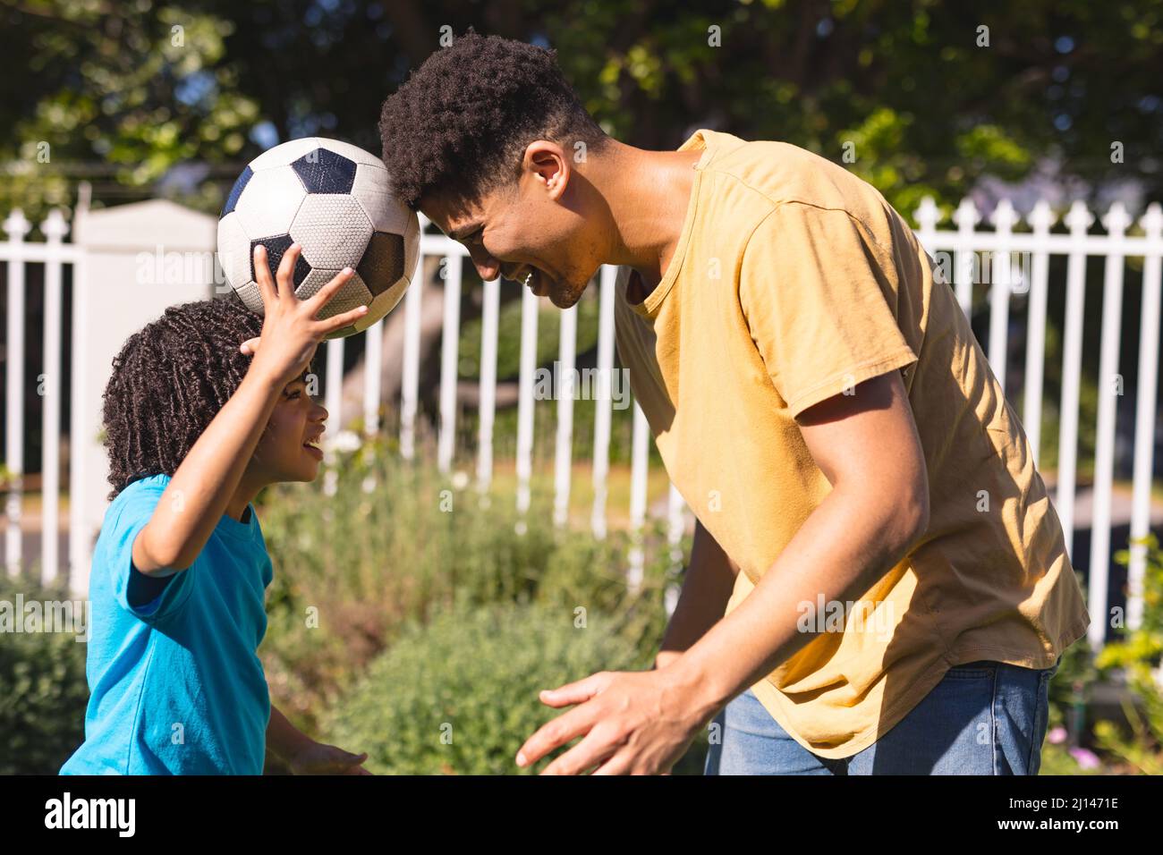 Side view of father and son playing with soccer ball at backyard on sunny day Stock Photo