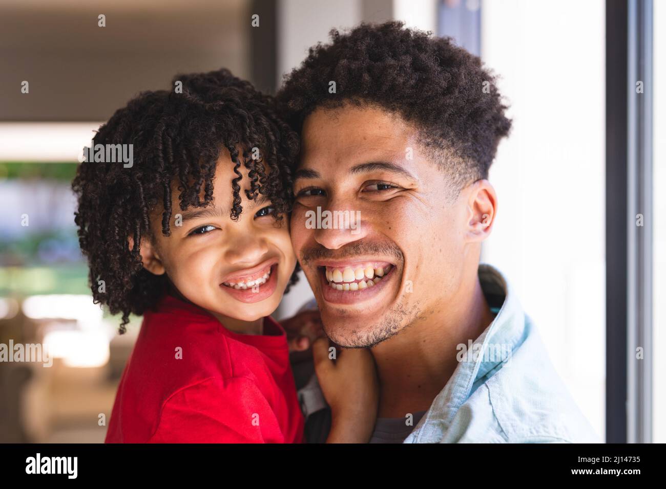 Portrait of cheerful hispanic father and son with curly black hair at home Stock Photo