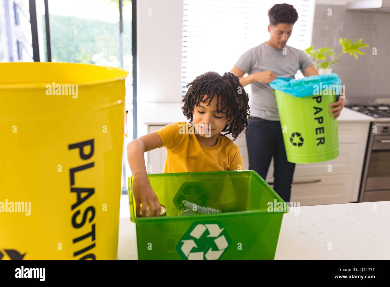 Hispanic boy collecting waste in recycling container with father at home Stock Photo