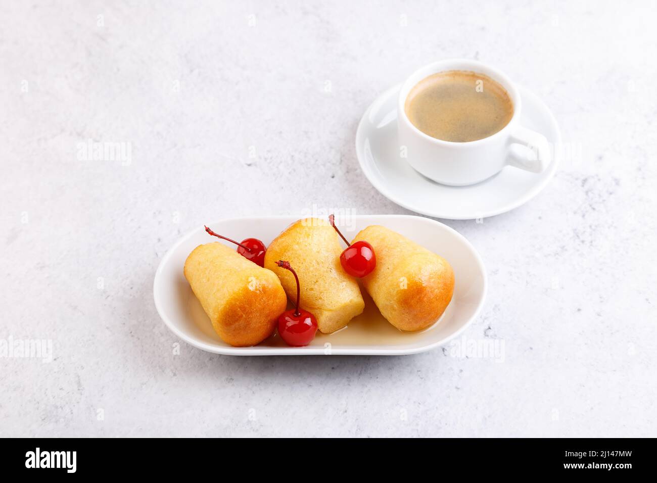 Neapolitan Rum baba (or baba au rum) on a white plate with a cocktail