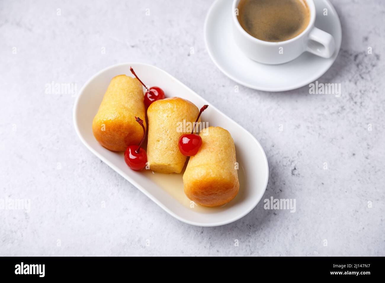 Neapolitan Rum baba (or baba au rum) on a white plate with a cocktail