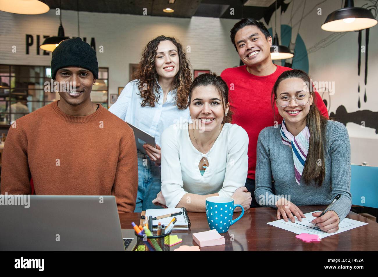 Smiling multiethnic coworkers looking at camera making team picture in multifunctional room of the pizza restaurant for working brunch - Diverse work Stock Photo
