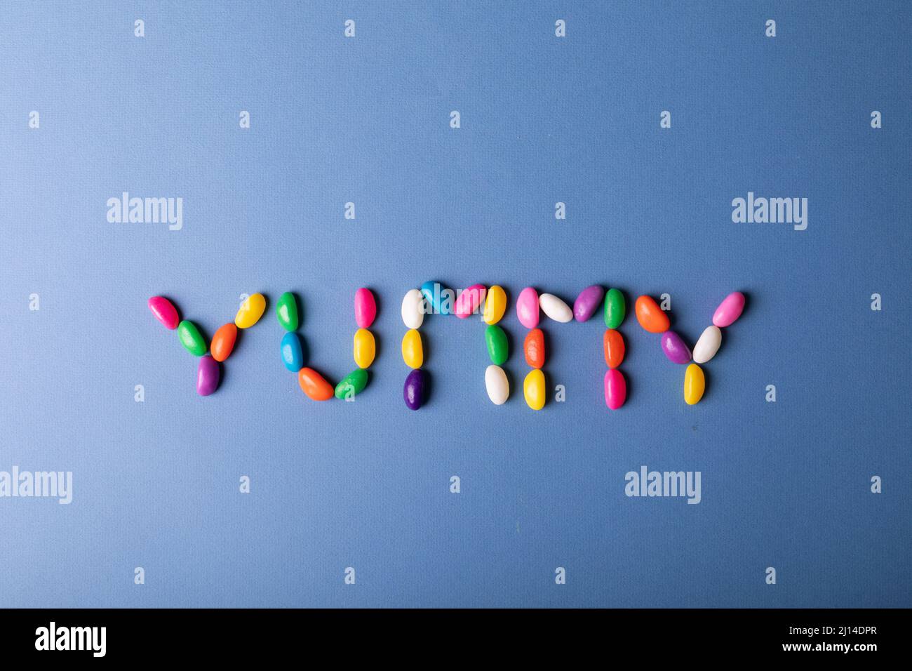 Overhead view of multi colored candies arranged as yummy word on blue background with copy space Stock Photo