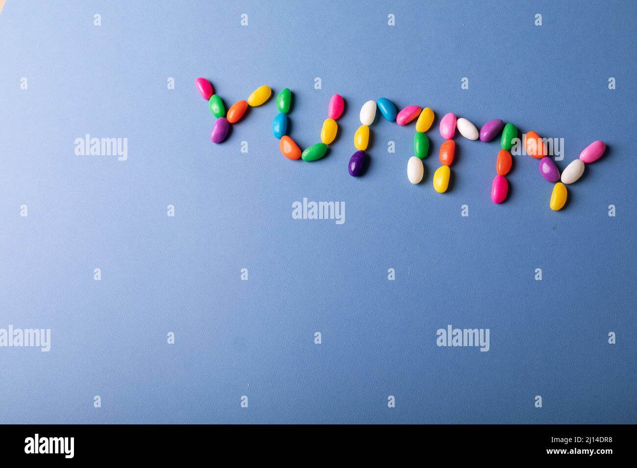 Overhead view of yummy word arranged from colorful candies on blue background over copy space Stock Photo