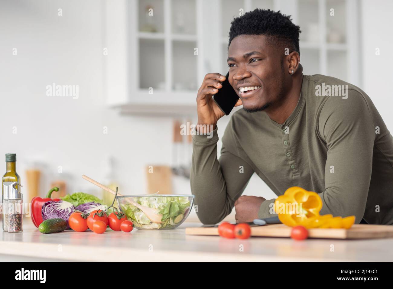 Mobile communication. Happy handsome black man talking on cellphone in kitchen Stock Photo