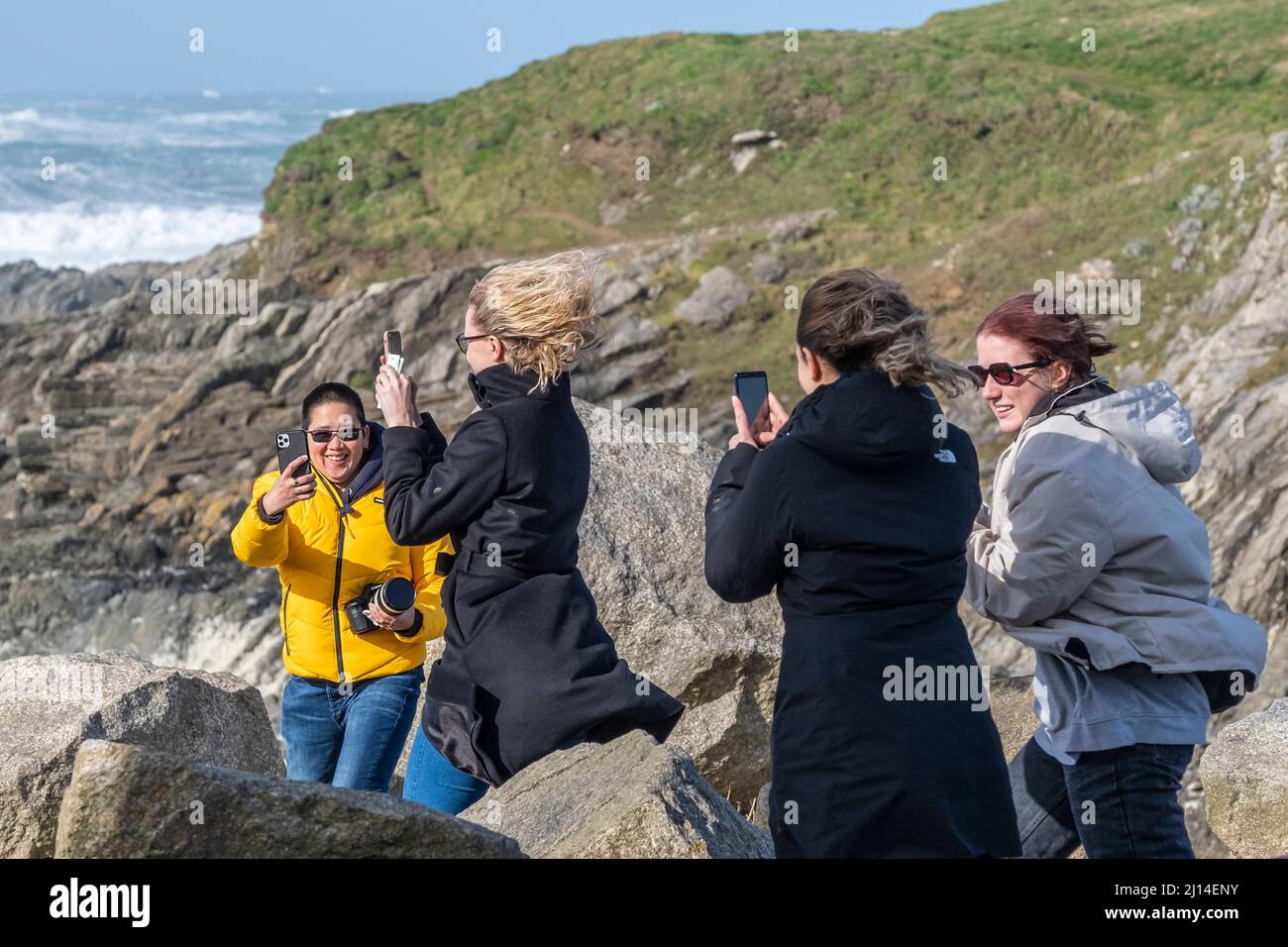 A group of friends using their mobile phones to record themselves in the storm force wind caused by Storm Eunice as it arrives on the North Cornwall c Stock Photo