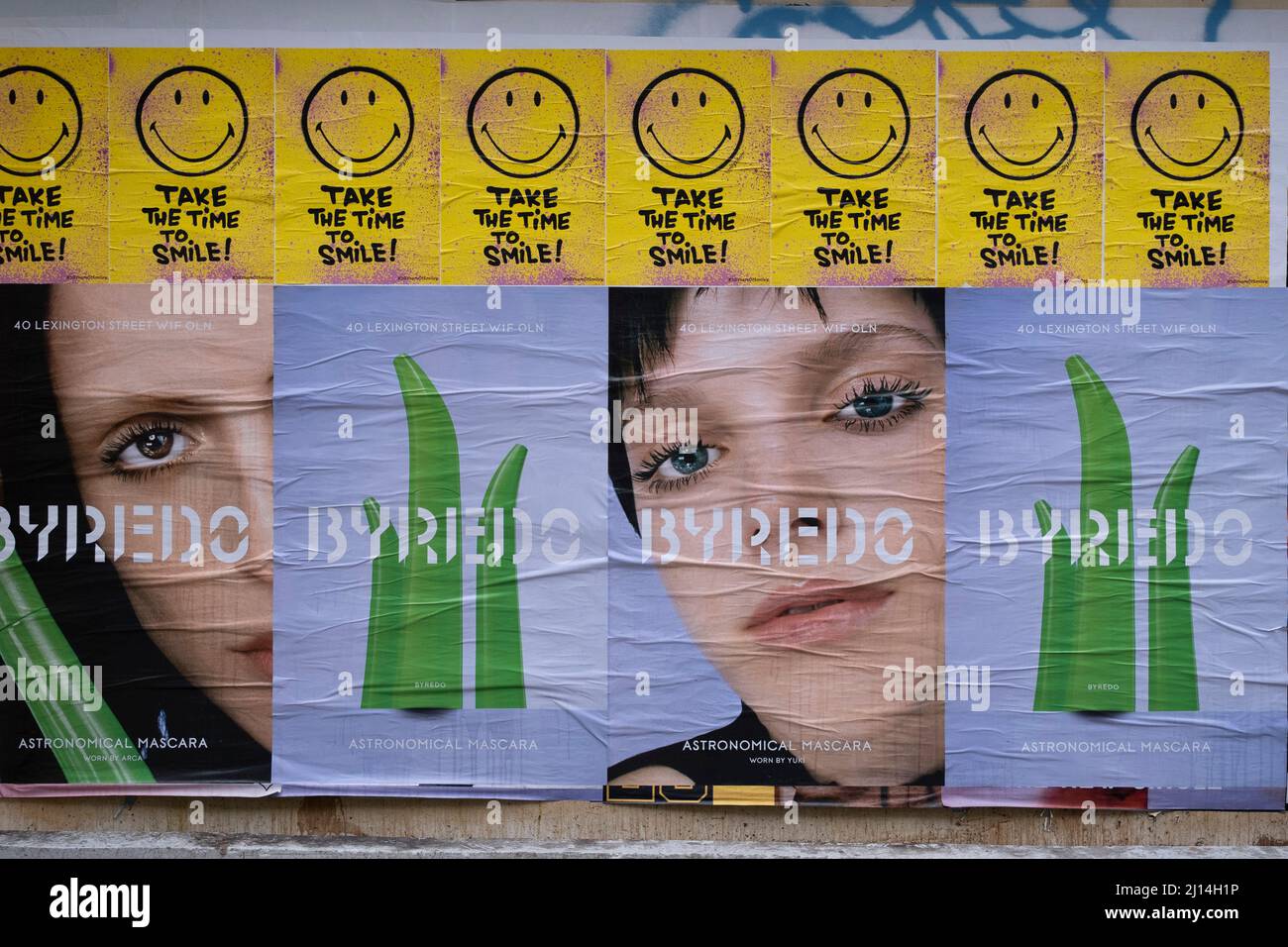 Take time to smile, smiley face posters above fashion make up company advertising posters on Berwick Street on 3rd March 2022 in London, United Kingdom. A smiley, sometimes called a happy face or smiley face, is a stylised representation of a smiling humanoid face that is a part of popular culture worldwide. The classic form designed by Harvey Ball in 1963 comprises a yellow circle with two black dots representing eyes and a black arc representing the mouth. Stock Photo