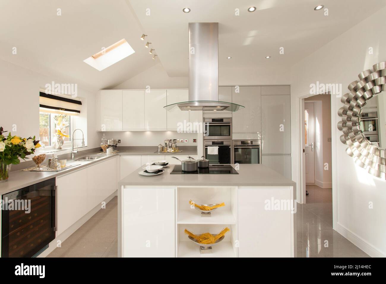 White kitchen in modern house home, centre island unit with hob and extractor hood, gloss units, tiled floor. Stock Photo