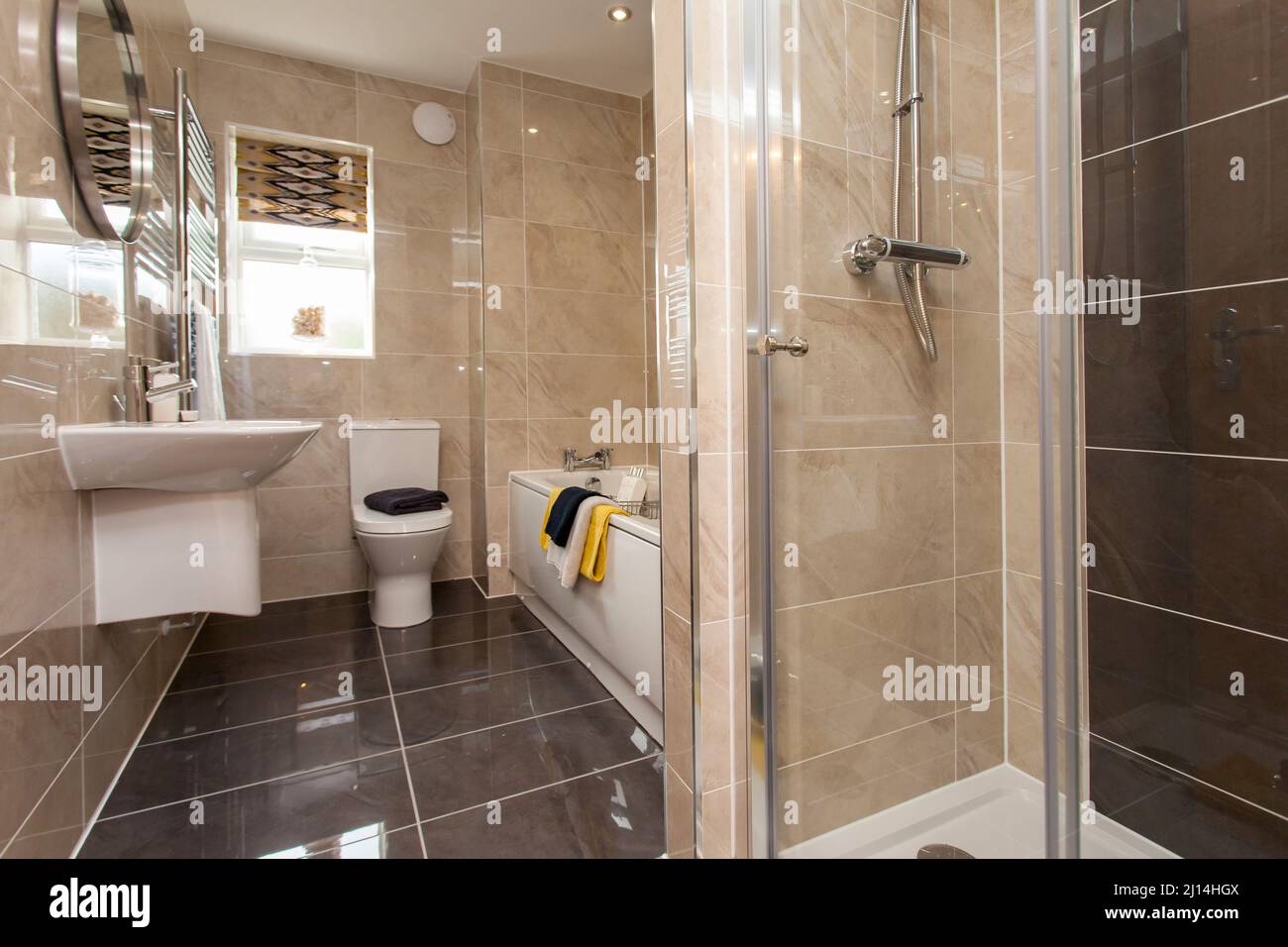 Modern bathroom with toilet, shower cubicle, wash basin sink, bath, tiled throughout. Stock Photo