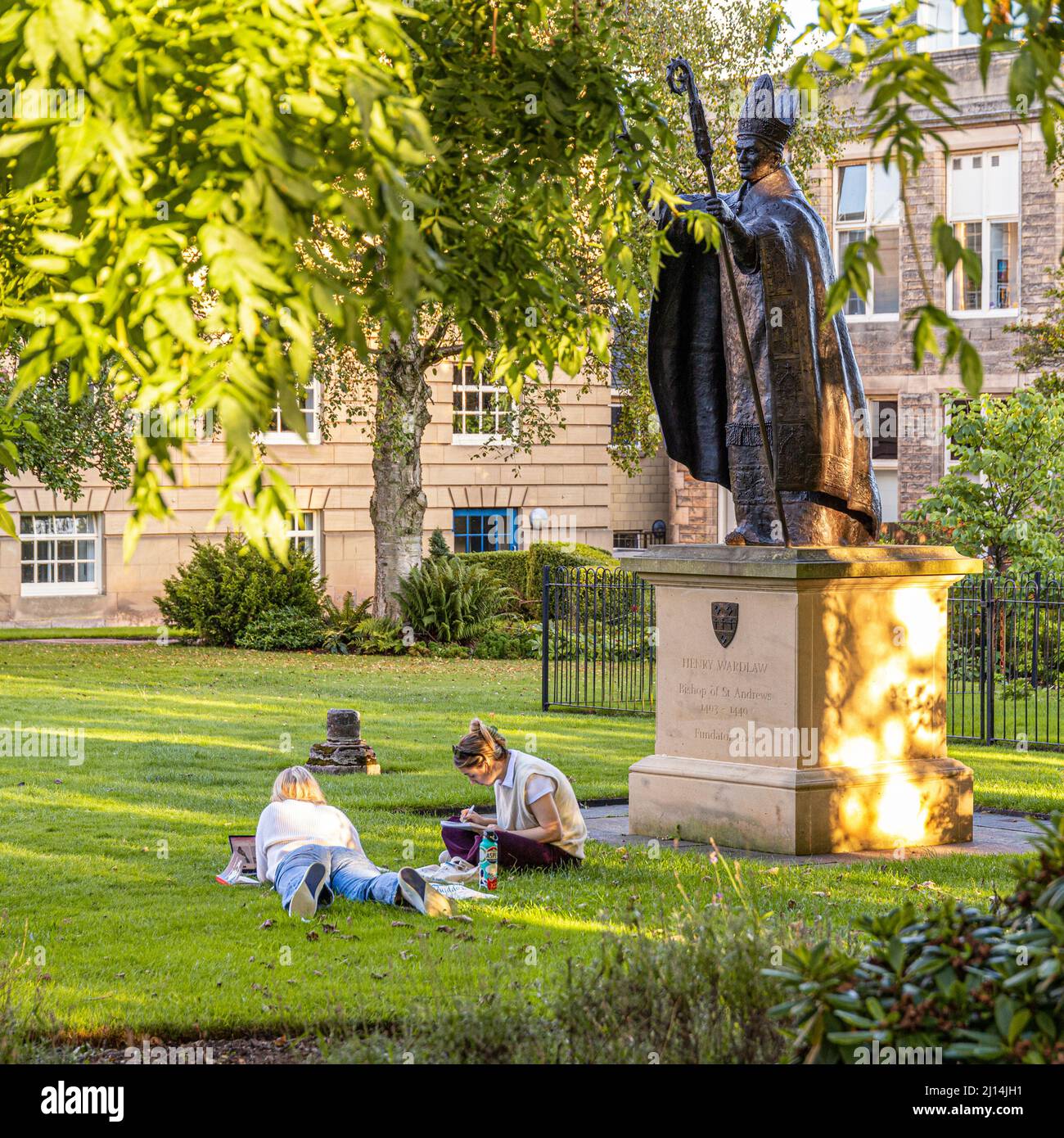 The statue of Bishop Henry Wardlaw watching over two female students studying in St Marys College Quadrangle, University of St Andrews, Fife, Scotland Stock Photo