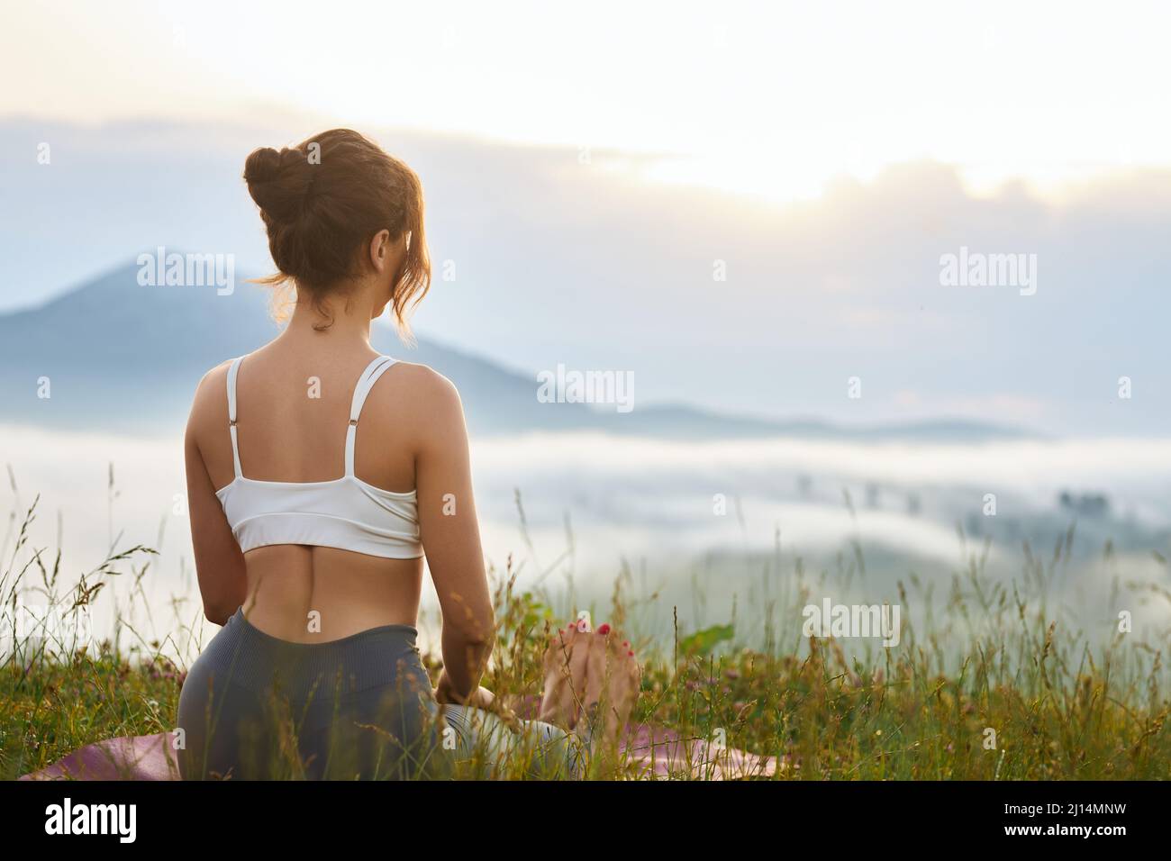 Back panoramic view of female sitting on legs with hands on knees. Woman looking forward, enjoying scenery, practicing yoga outdoors. Concept of harmo Stock Photo