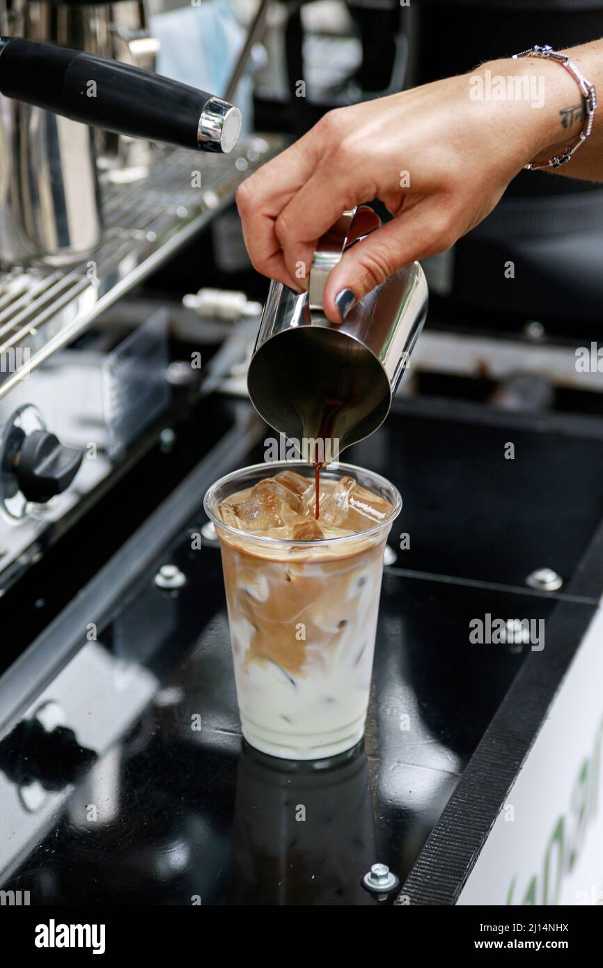 Preparing iced coffee. Pouring coffee into the glass with milk and ice