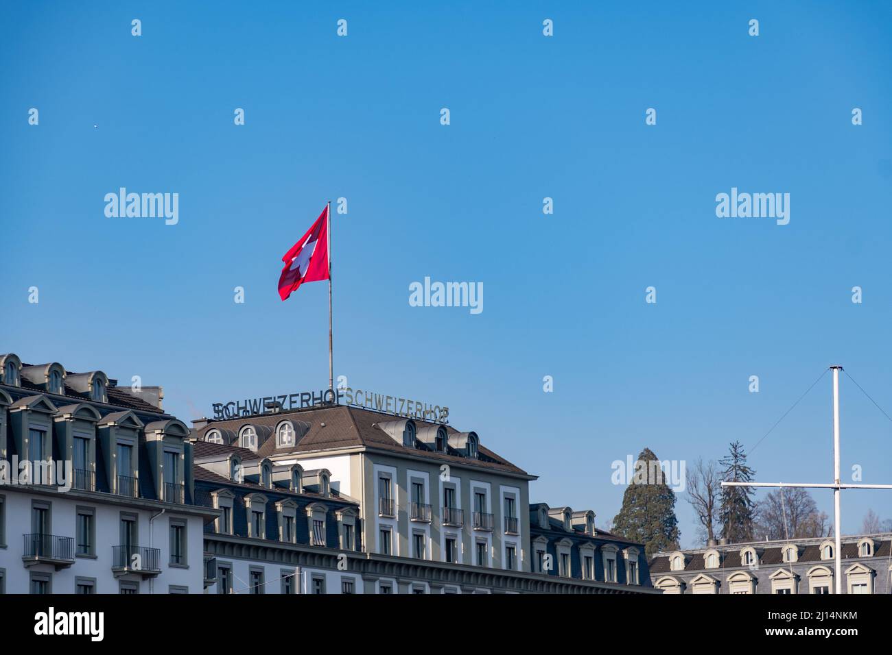 Lucerne, Switzerland, March 10, 2022 Waving swiss flag on the roof top of a hotel Stock Photo